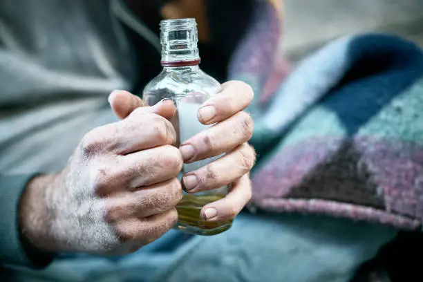 Photo of Hands of an alcoholic homeless man clutching bottle