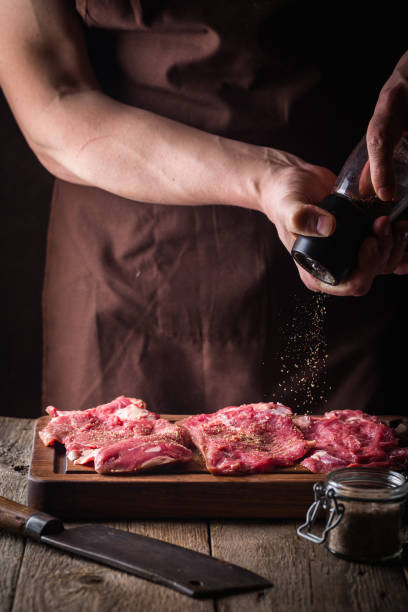 Man cooking meat steaks Man cooking meat steaks on kitchen. Chef salt and pepper meat on wooden background cut of meat stock pictures, royalty-free photos & images