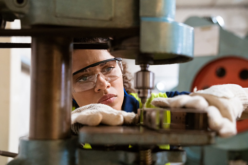 Close-up of female apprentice using yoke machine. Female engineer is wearing protective glasses in factory. She is working in manufacturing industry.