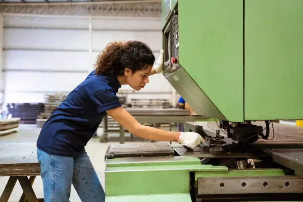 Serious female engineer using puller machine at factory. Mid adult trainee is wearing uniform. She is working in manufacturing industry.