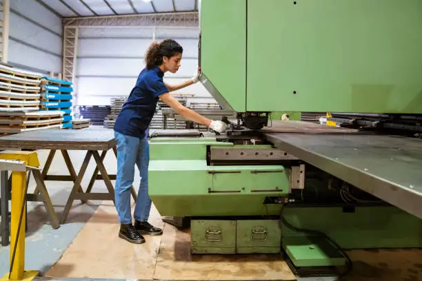 Female engineer using puller machine. Full length of mid adult apprentice is working in manufacturing factory. She is in uniform at industry.