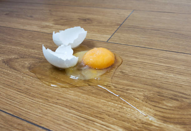 A broken egg on a wooden kitchen's floor. Selective focus, close-up.