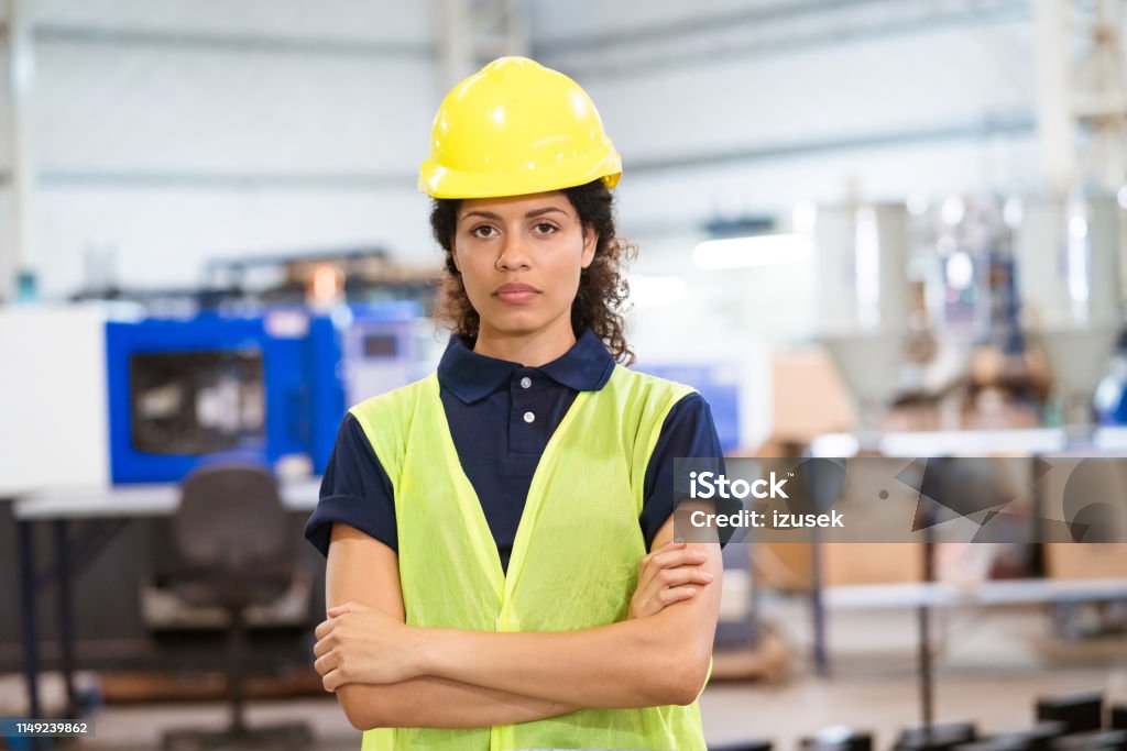 Portrait of engineer in hardhat with arms crossed Portrait of female apprentice wearing hardhat. Mid adult engineer is standing with arms crossed. She is in reflective clothing at factory. 30-34 Years Stock Photo