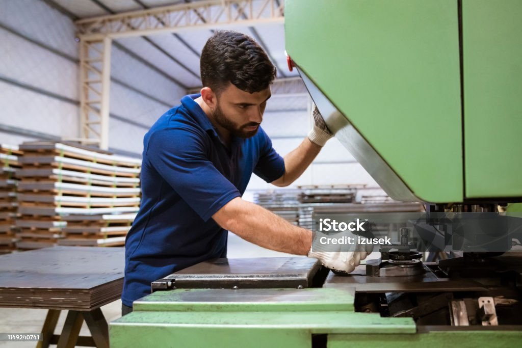 Engineer using puller machine in industry Young engineer using puller machine. Male apprentice is working in manufacturing factory. He is wearing uniform. 20-24 Years Stock Photo