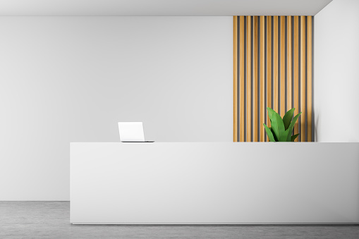 White reception desk with laptop on it standing in modern office with white and wooden walls and concrete floor. 3d rendering