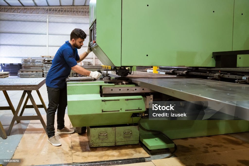 Manual worker using puller machine in industry Full length of male engineer using puller machine. Young trainee is working in manufacturing industry. He is in uniform at factory. Full Length Stock Photo