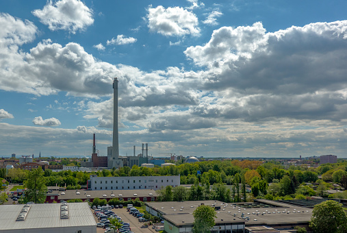 Aerial view of the caravans of the carnies standing behind the rides of a fairground. A combined heat and power plant with a long chimney in the back, above