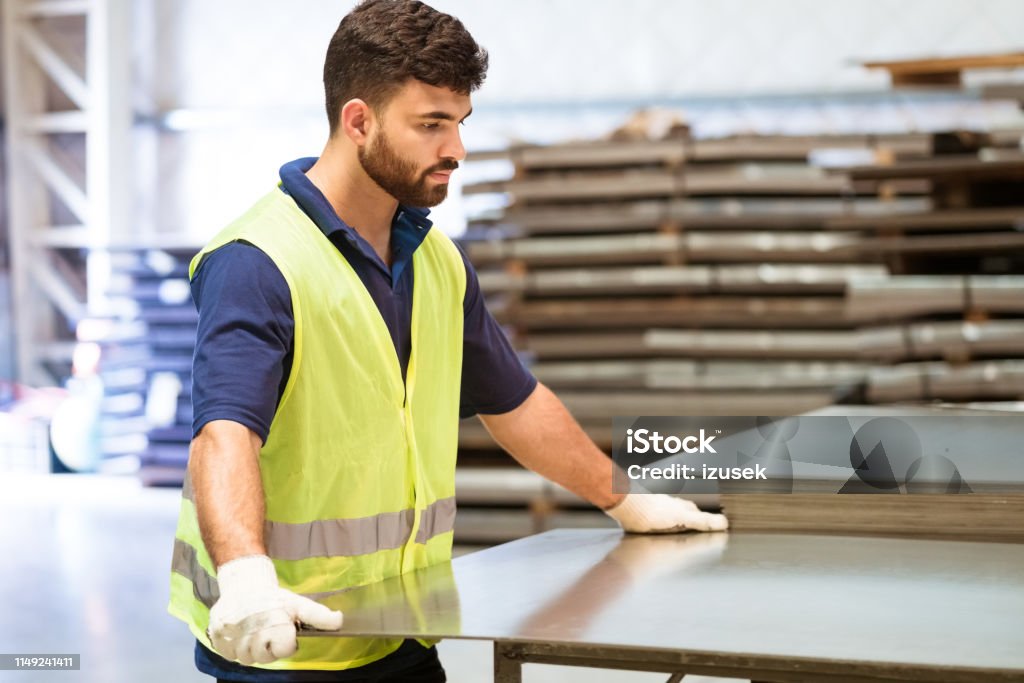 Serious engineer adjusting metal sheet in industry Serious young engineer adjusting metal sheet on machinery. Male apprentice is in protective workwear. He is working in manufacturing industry. 20-24 Years Stock Photo