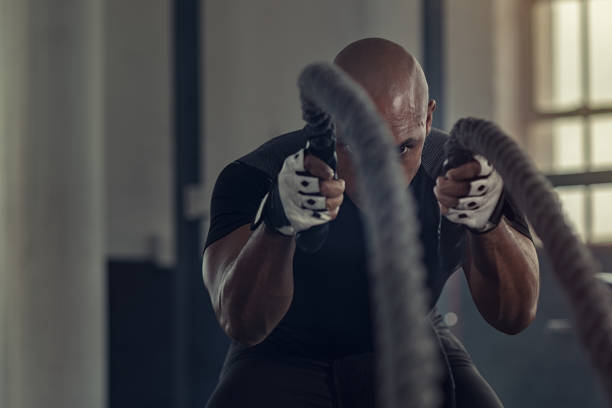 Black man doing intensive battle rope workout Strong athlete doing exercises with rope at cross training gym. Bald african man working out with ropes at gym gym. Fitness strong man pulling rope at fitness center. gym men africa muscular build stock pictures, royalty-free photos & images