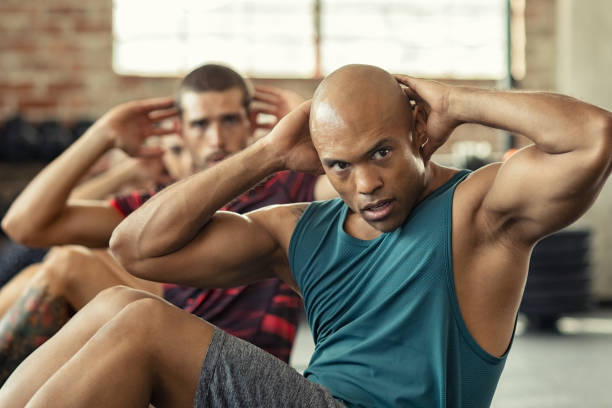 Men doing sit ups workout Muscular african american man doing sit ups at gym with other people in background. Mature black man doing abs workout with class at cross training gym. Muscular guy doing crunches. sit ups stock pictures, royalty-free photos & images