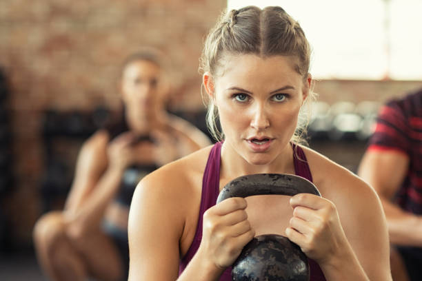 donna fitness determinata che fa squat con campana bollitore - kettle bell sport women muscular build foto e immagini stock