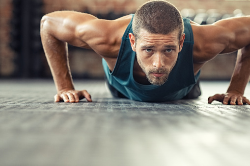 Young athlete doing push ups as part of bodybuilding training. Muscular guy doing a pushup on floor at cross training gym. Determined athletic guy in sportswear exercising.