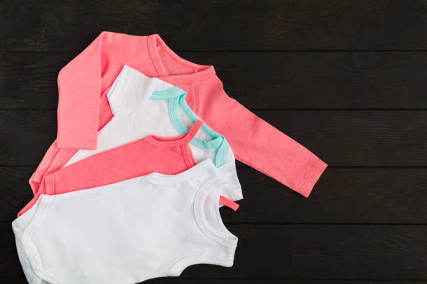 istock Pink and white babysuits over brown wooden background with copy space. Flat lay style 1149247337