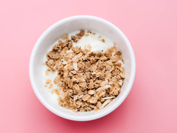 istock Whole grains on yogurt in white bowl, pink background. 1149247350