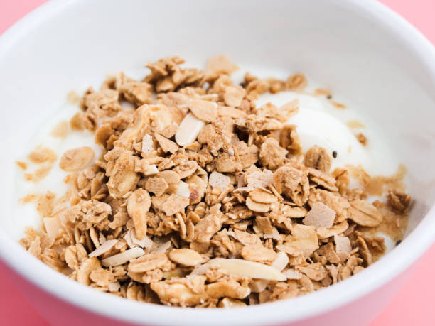istock Whole grains on yogurt in white bowl, pink background. 1149248527