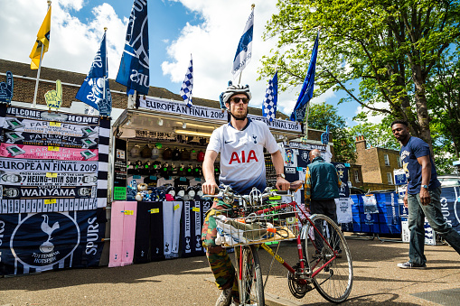 London, UK - 12 May, 2019: color image depicting Tottenham Hotspur football fans perusing and buying items from a Spurs merchandise stall outside the stadium in north London, UK, on a Premier League match day. It is the day of an English Premier League match (Tottenham v Everton). The items for sale include blue and white team scarves, pin badges and keyrings, hats and t shirts. Room for copy space.