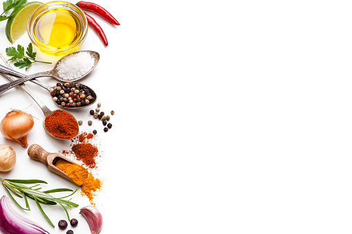Cooking and seasoning backgrounds: High angle view of a white background with multi colored vegetables, herbs and spices placed at the left border making a frame and leaving a useful copy space for text and/or logo at the center. The composition includes olive oil, cherry tomatoes, lime slice, red onion, parsley, star anise, garlic, salt, pepper, chili pepper, turmeric and gold onions. High key DSRL studio photo taken with Canon EOS 5D Mk II and Canon EF 100mm f/2.8L Macro IS USM.