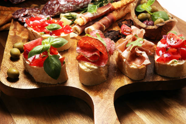 istock Traditional italian antipasto bruschetta appetizer with cherry tomatoes, cream cheese, basil leaves and balsamic vinegar on cutting board with prosciutto, salami, cheese 1149257559