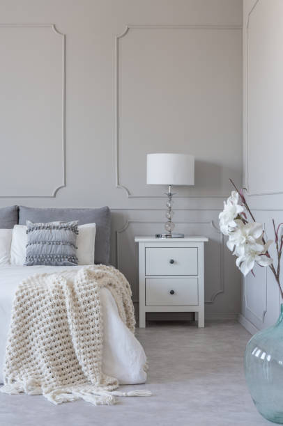 istock Simple white lamp on wooden night stand table with two drawers next to comfortable king size bed with cozy bedding 1149261794