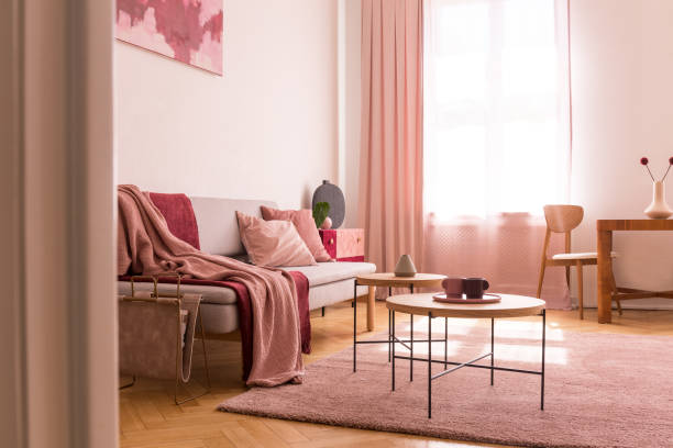 istock Pink blanket on sofa next to tables on purple carpet in flat interior with drapes at window. Real photo 1149264186
