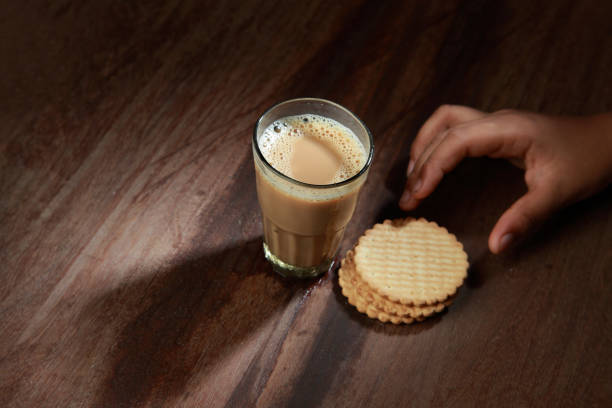 istock A glass of tea and biscuits on a wooden table with a human hand 1149267348