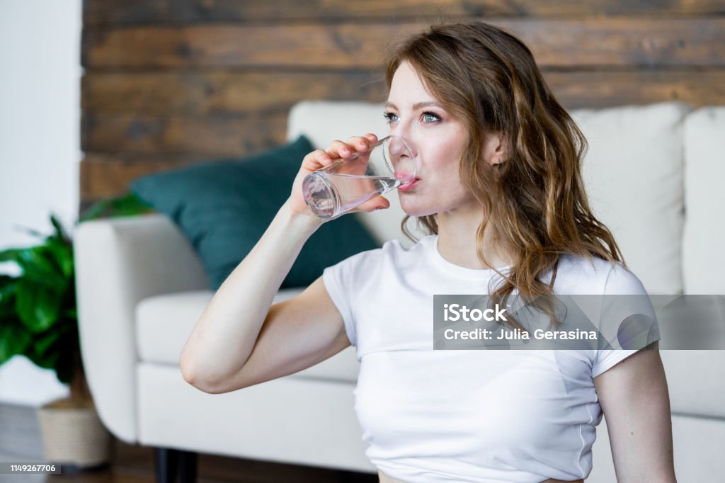 Young blonde woman drinking water after doing stretching yoga exercises at home. Young blonde woman drinking water after doing stretching yoga exercises at home. Healthy lifestyle. Activity Stock Photo