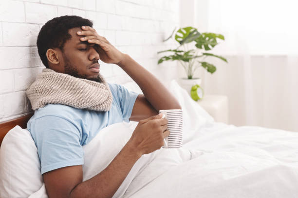 Sick african-american man drinking hot healing tea in bed Feeling bad. Sick african-american man drinking hot healing tea in bed, touching his forehead, empty space cold and flu man stock pictures, royalty-free photos & images