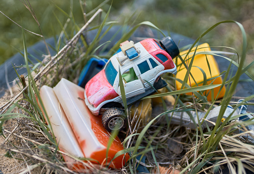 Worn and broken toys (cars and cubes) piled on the ground lie in the backyard. Shooting on a back yard of a country cottage at a sunny spring day