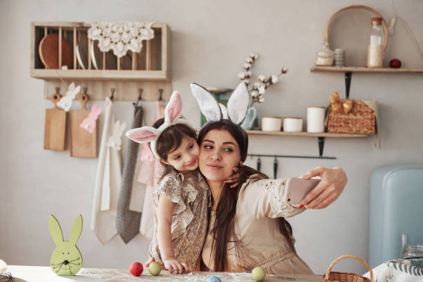 tomando selfie. madre e hija en las orejas de conejo en la época de pascua tienen un poco de diversión en la cocina durante el día - vacations two generation family holiday easter fotografías e imágenes de stock