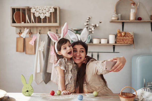 haciendo caras graciosas. madre e hija en las orejas de conejo en la época de pascua tienen un poco de diversión en la cocina durante el día - vacations two generation family holiday easter fotografías e imágenes de stock