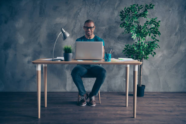 istock Full length body size photo amazing he him his macho handsome notebook table lamp light green plant reliable person excited duty wear specs blue t-shirt pants sit chair indoors workstation office 1149277562