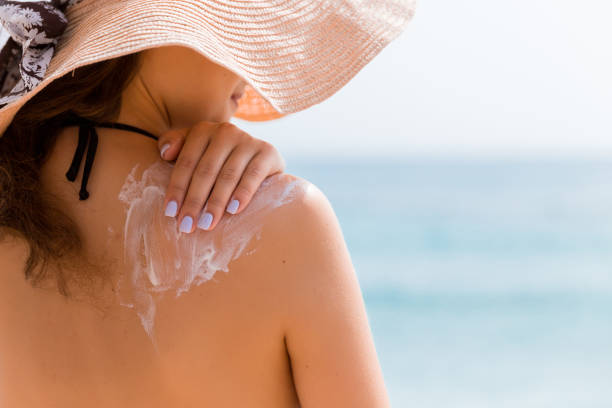 young girl in straw hat is applying sunscreen on her back to protect her skin - shoulder bone imagens e fotografias de stock