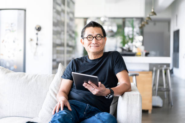 istock Mature Chinese man sitting on sofa with a digial tablet in hand 1149279280