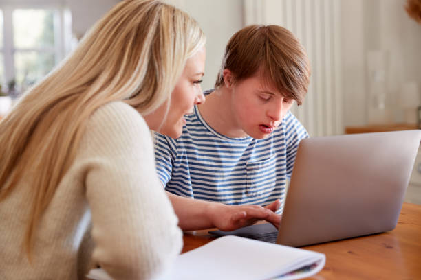 sindrome di downs uomo seduto con tutor di casa usando laptop per lezione a casa - working physical impairment people occupation foto e immagini stock