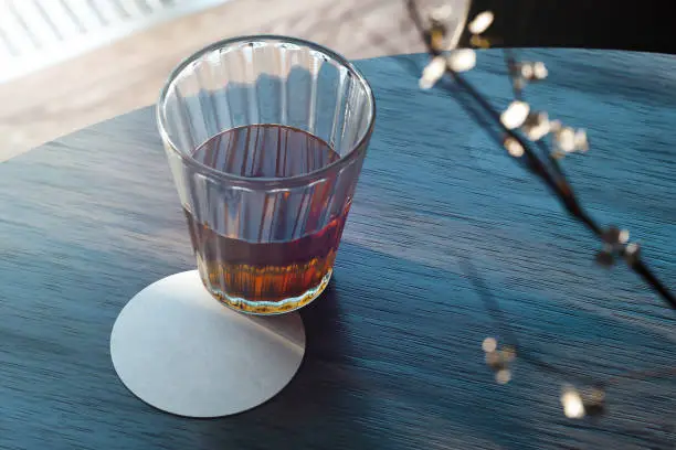 Transparent realistic glass with tea and beer coaster on wooden table. 3d rendering.