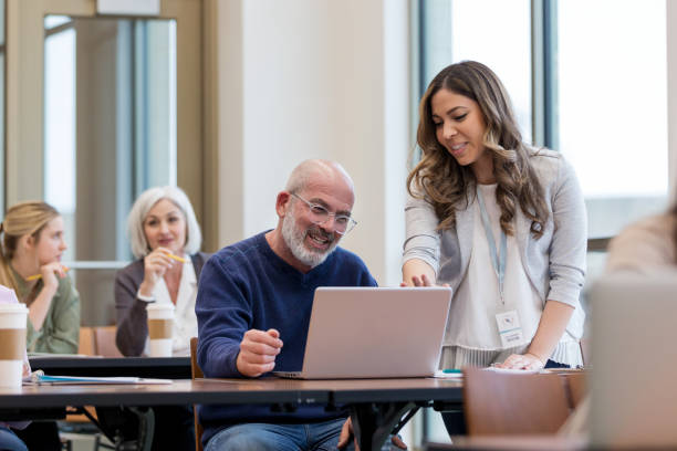 istock Mid adult teacher points to computer to help student 1149286183