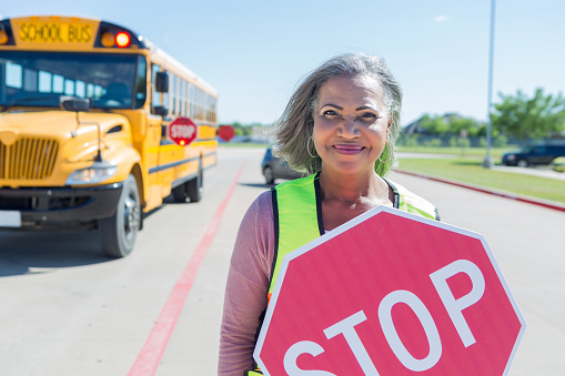 A pleasant cheerful African American grandmother serves as a crossing guard to keep children safe.