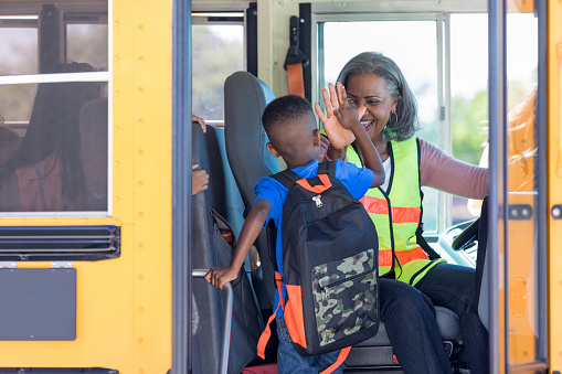 On the first day of school, a mature adult bus driver welcomes a new first grader by giving him a high five.