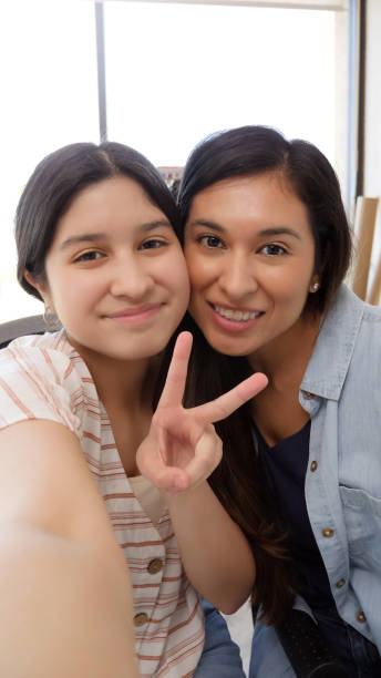 Hispanic mom and daughter use smart phone for selfie