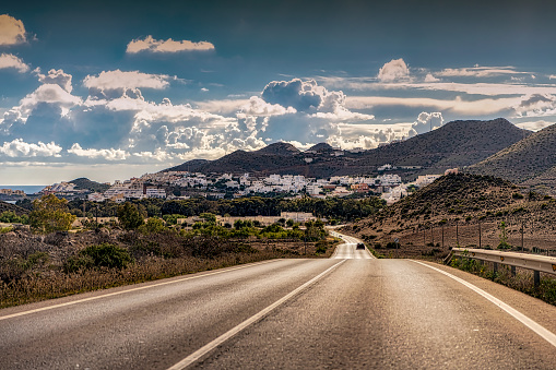 Cloudy sky over Cabo de Gata highway and distant white village on the Mediterranean coast of Spain.
