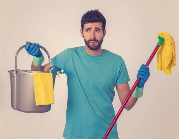 Young attractive man tired and upset holding bucket mop and cleaning spray feeling sad frustrated and lazy in domestic duties concept and men and women gender roles. Isolated on blue background joven atractivo hombre cansado y molesto sosteniendo la fregona del cucharón y aerosol de limpieza sintiéndose triste frustrado y perezoso en el concepto de deberes domésticos y hombres y mujeres roles de género. aislado sobre fondo azul