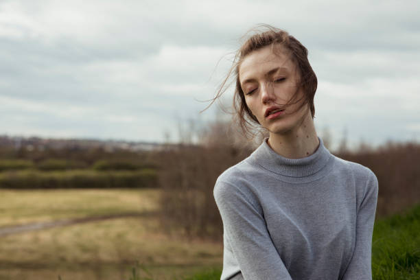 Portrait of young woman with hair blown by wind outdoors. Head and shoulders shot with eyes closed.