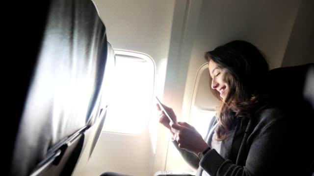 Young woman laughs while using smartphone during flight