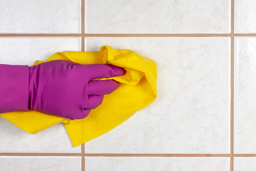 A gloved hand holds a rag and washes ceramic tiles