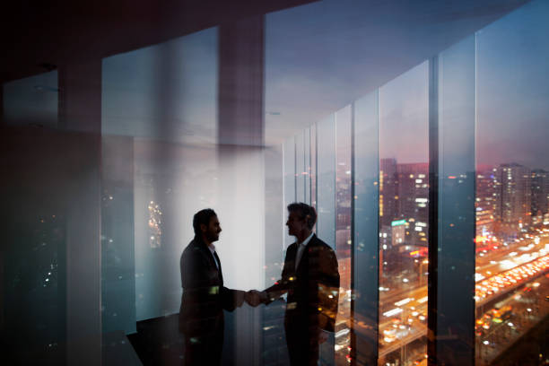 empresarios sacudiendo las manos en la oficina por la noche - night cityscape reflection usa fotografías e imágenes de stock