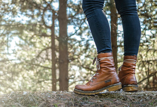 Female legs with leather boots close up view in forest, unfocused trees on background. Hiking tourism conept. Forest in the mountains.