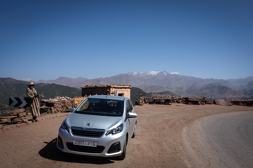 Aguelmouss, Morocco - March 19th, 2019: High Atlas Mountains outlook with a Maroccan selling some herbs and a compact car