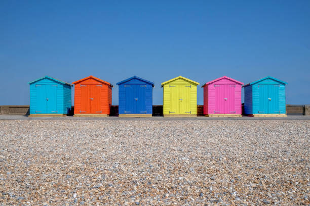 a line of six colorful beach huts A line of six brightly coloured Beach huts, each one is a different colour in the foreground is a pebble beach and behind is a bright blue sky, Seaford, east Sussex, England, United Kingdom, UK, beach hut stock pictures, royalty-free photos & images