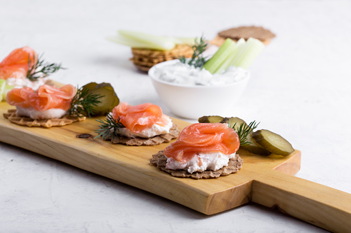 Party food, appetizer with salmon pate and smoked salmon, yoghurt dip with dill, celery sticks and pickles on wooden board, snack platter close-up, selective focus