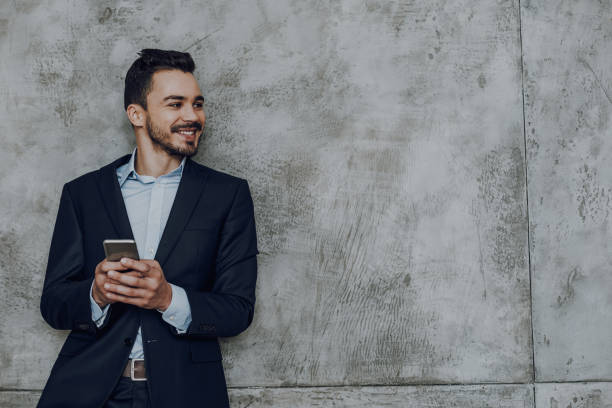 istock Cheerful man is spending time with smartphone against grey wall 1149340704